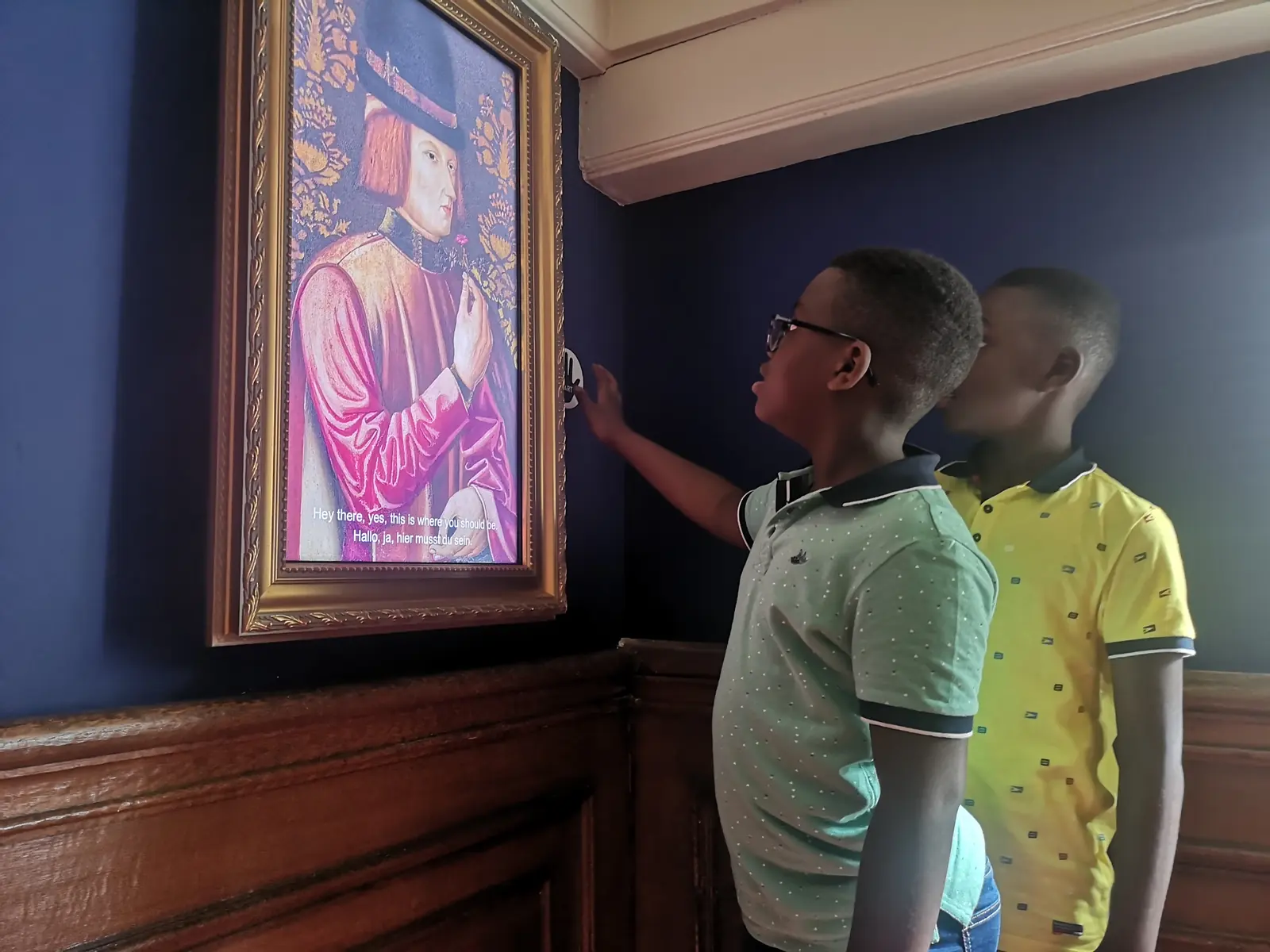 Two boys look at a painted portrait in a gilded frame that appears to speak on a screen.