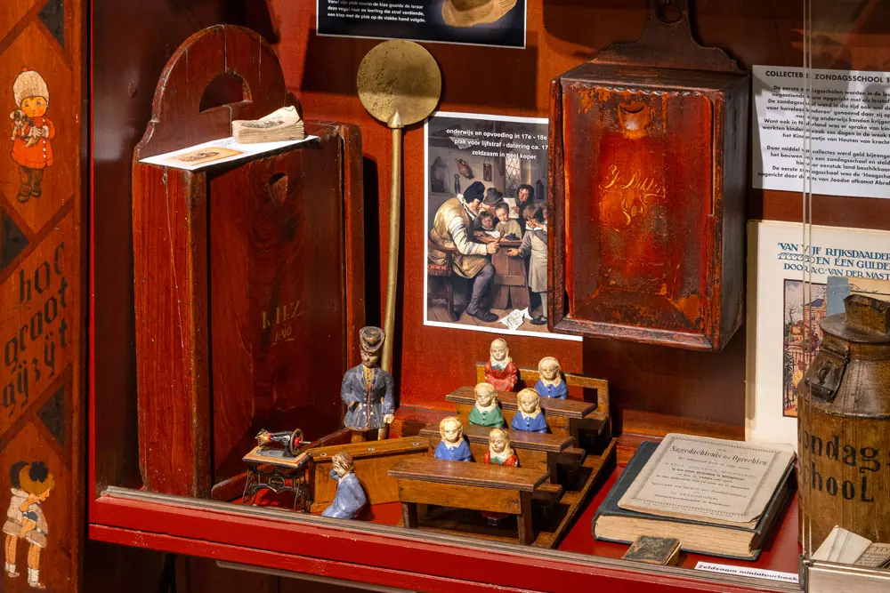 Eine Vitrine mit einem Miniatur-Klassenzimmer aus Püppchen in Tracht, einer Schultafel und Holzkästchen.