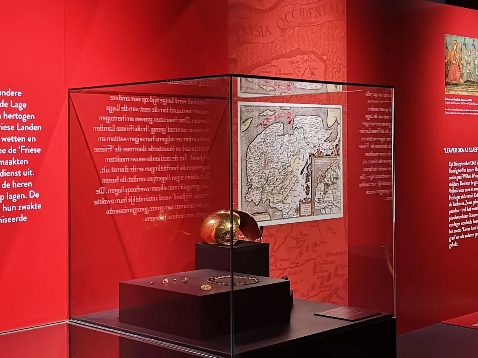 A glass display case in front of a red wall with an old map of Friesland and texts on Frisian history.