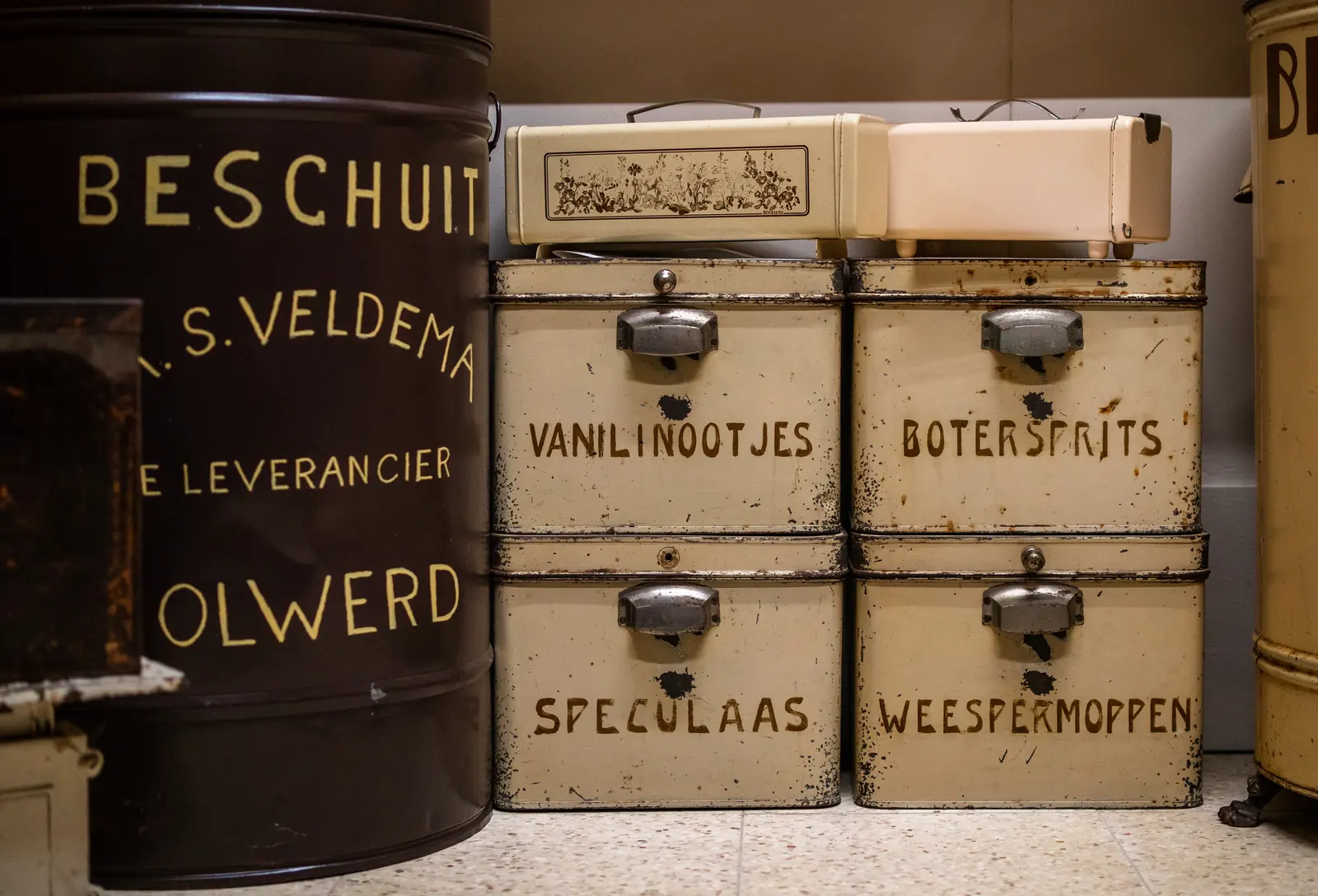D’anciennes boîtes de magasin portant des inscriptions comme beschuit, speculaas, vanillinootjes et boterspritsen.