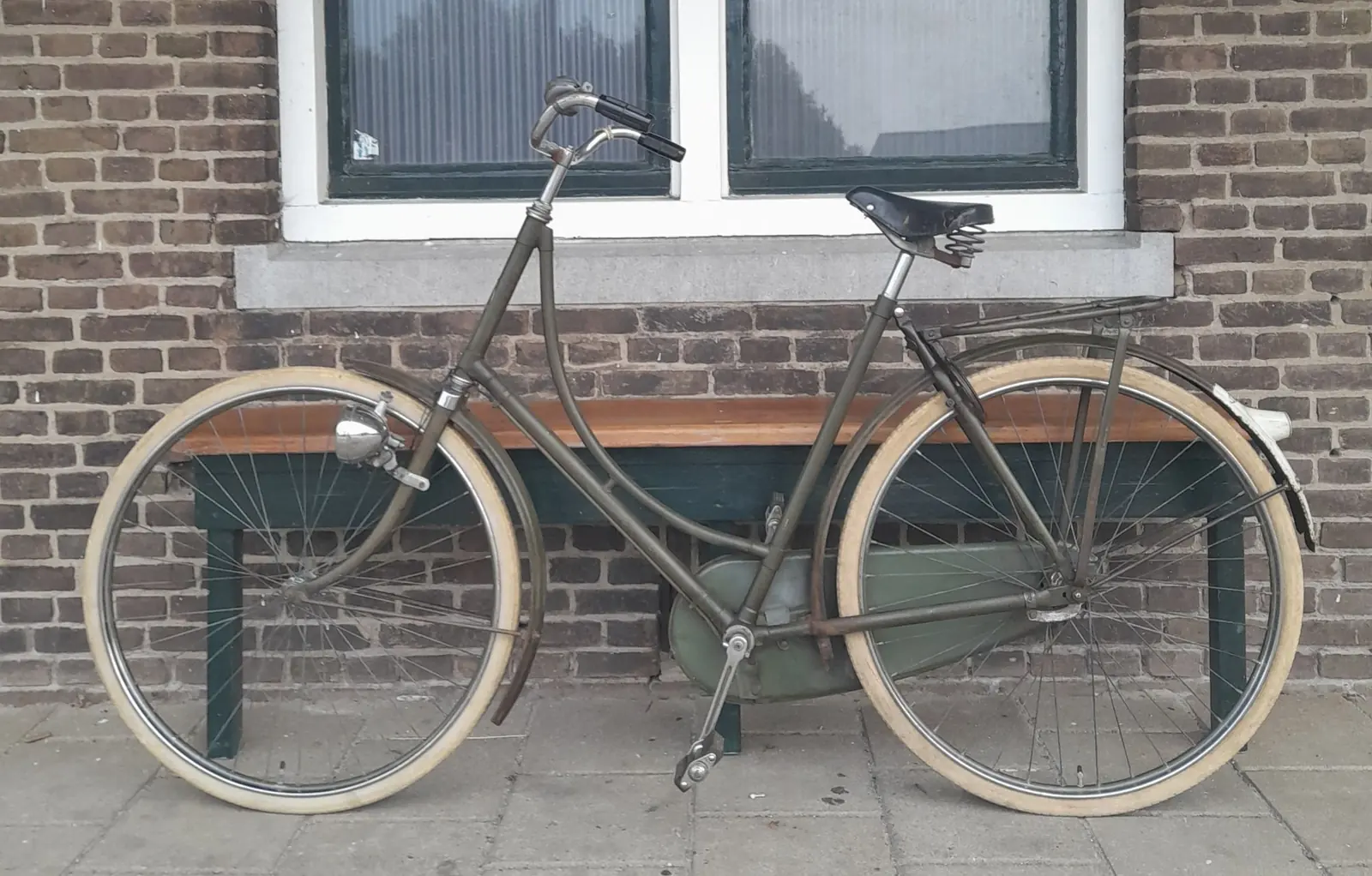 An old black lady’s bicycle leaning against a brick wall below a window.
