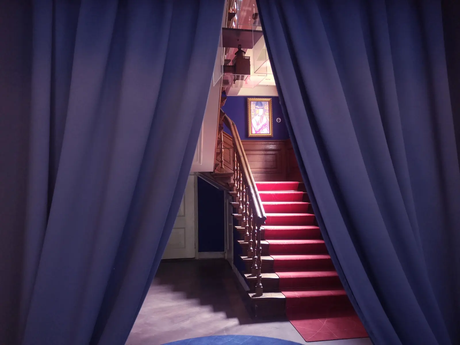 Between blue curtains you look onto a staircase with a red runner.