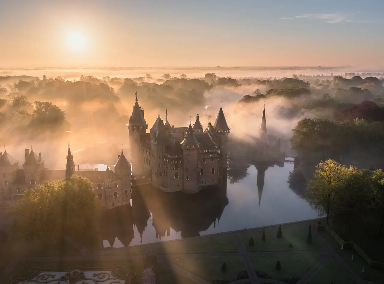 Luchtfoto van Kasteel de Haar bij zonsopkomst, omringd door water, bomen en ochtendnevel.