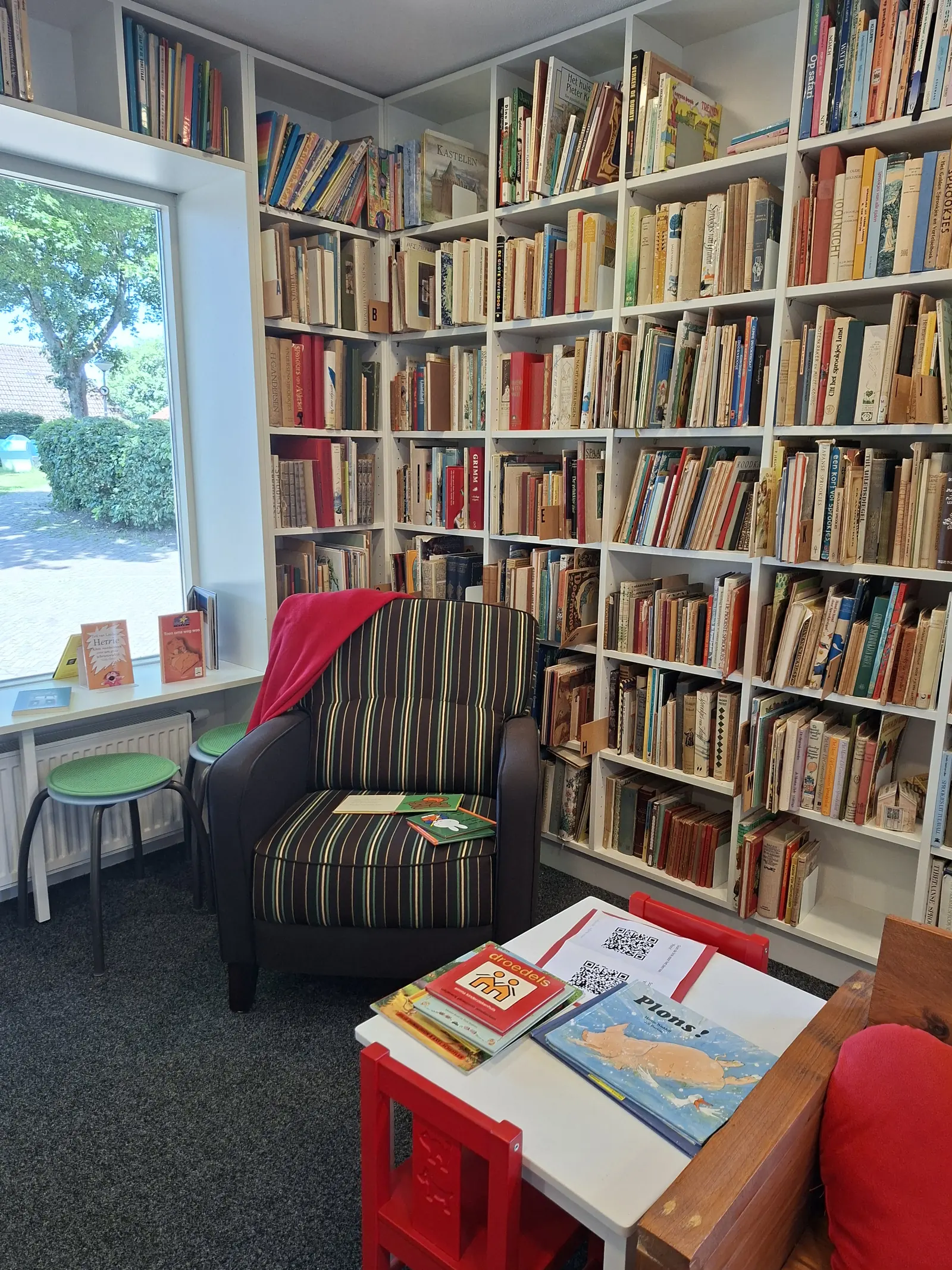 Un coin lecture avec un fauteuil rayé près de la fenêtre, entre des étagères remplies de livres.