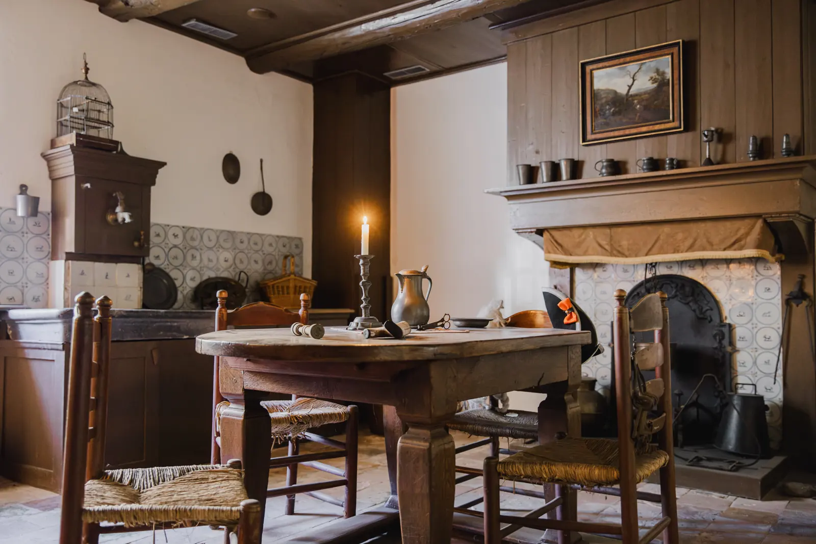 Interieur van de Kapiteinswoning in Bourtange: een tafel met stoelen, een schouw met een schilderij en tinnen kannen.