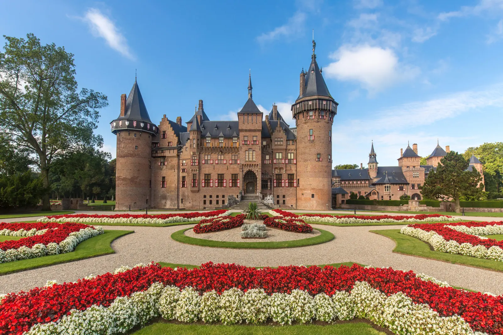 Kasteel de Haar met torens en spitsen, gezien over een plein met perken vol rode en witte bloemen.