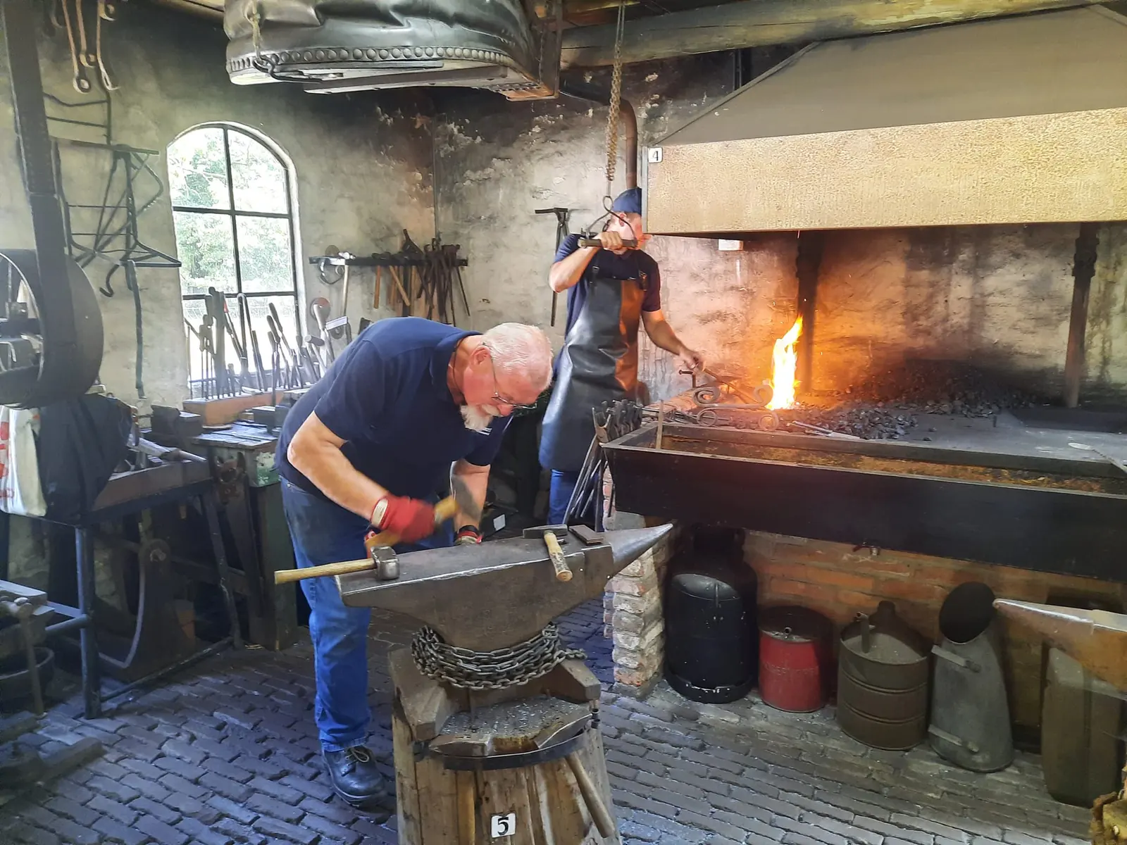 A blacksmith works glowing iron on an anvil in a forge with an open fire.