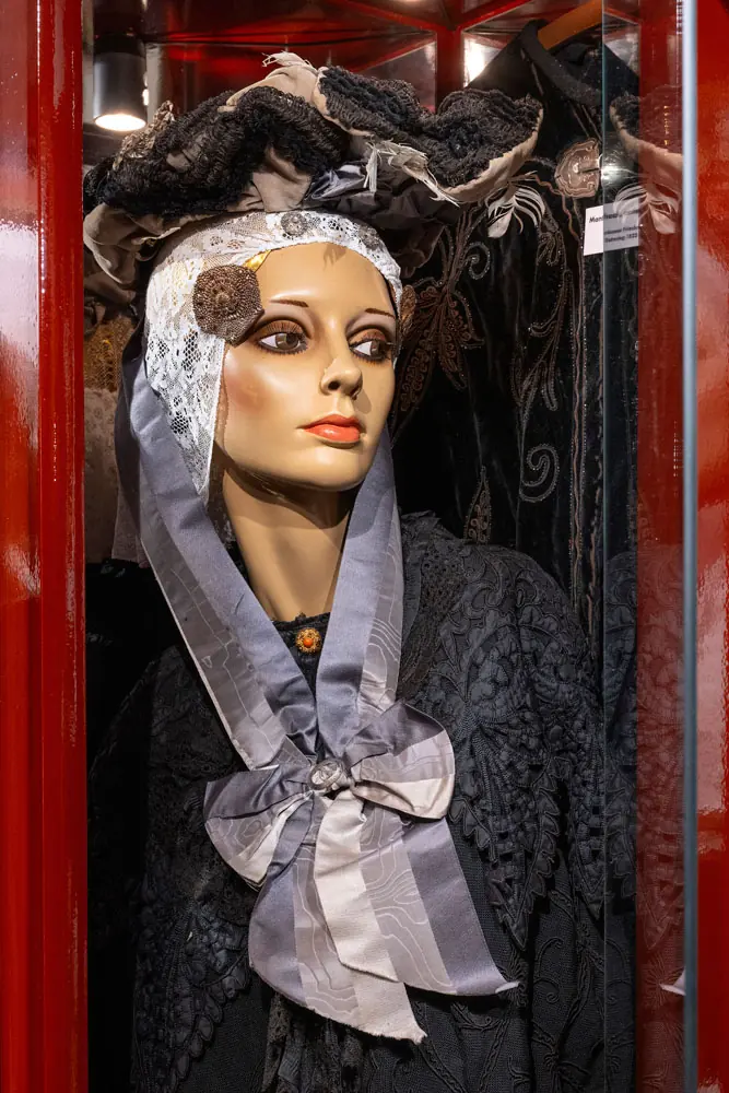 Eine Schaufensterpuppe mit schwarzer Haube und hellem Spitzentuch, mit einer Brosche geschmückt.