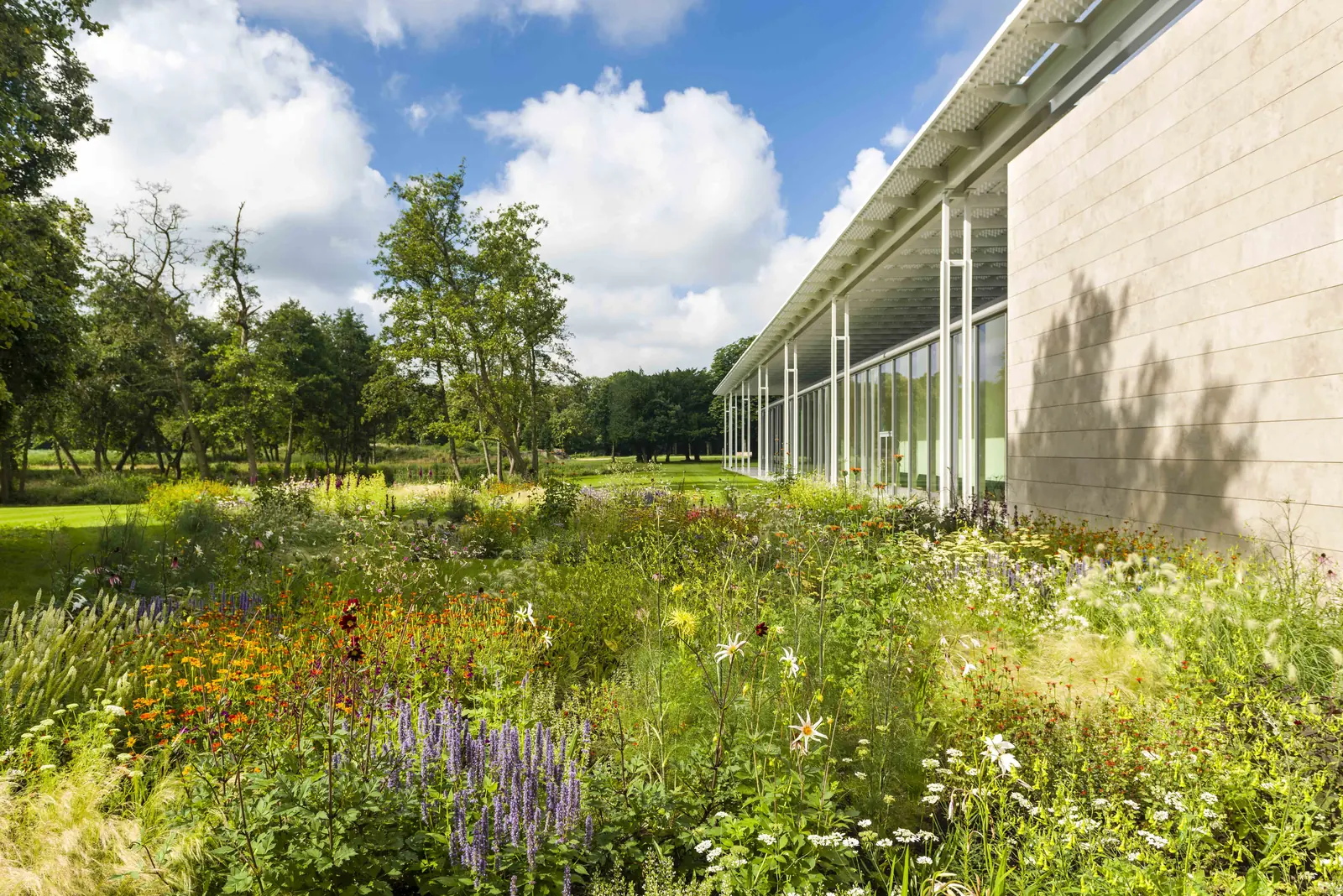 Een bloeiende border met grassen en vaste planten langs de gevel van het museum.