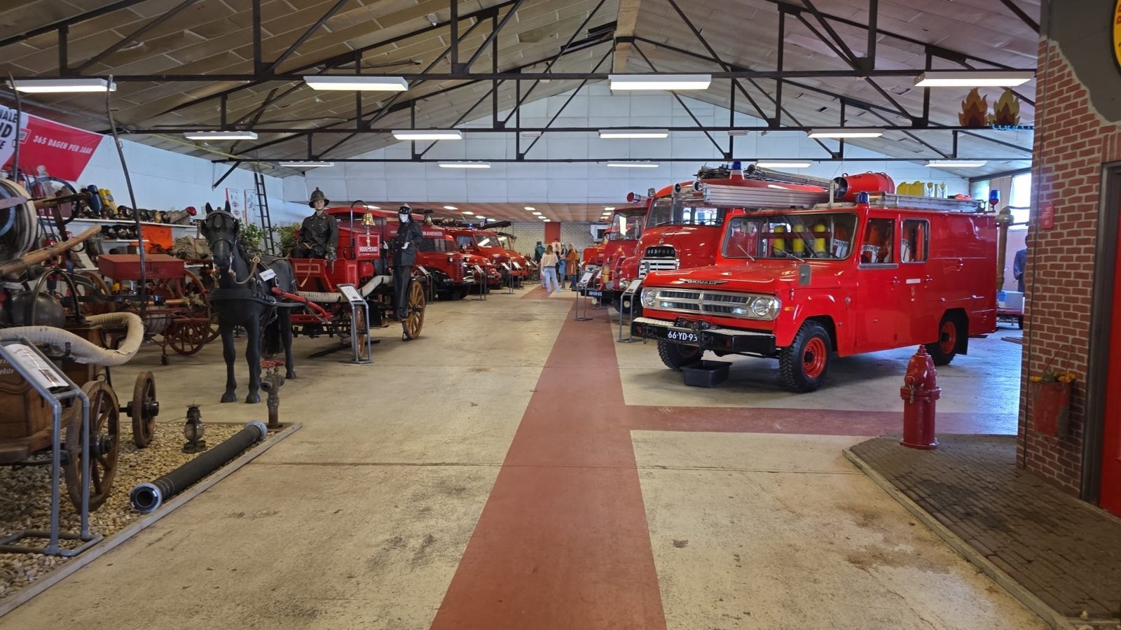 Vue intérieure d’un hall de musée avec des camions de pompiers rouges et une voiture hippomobile.