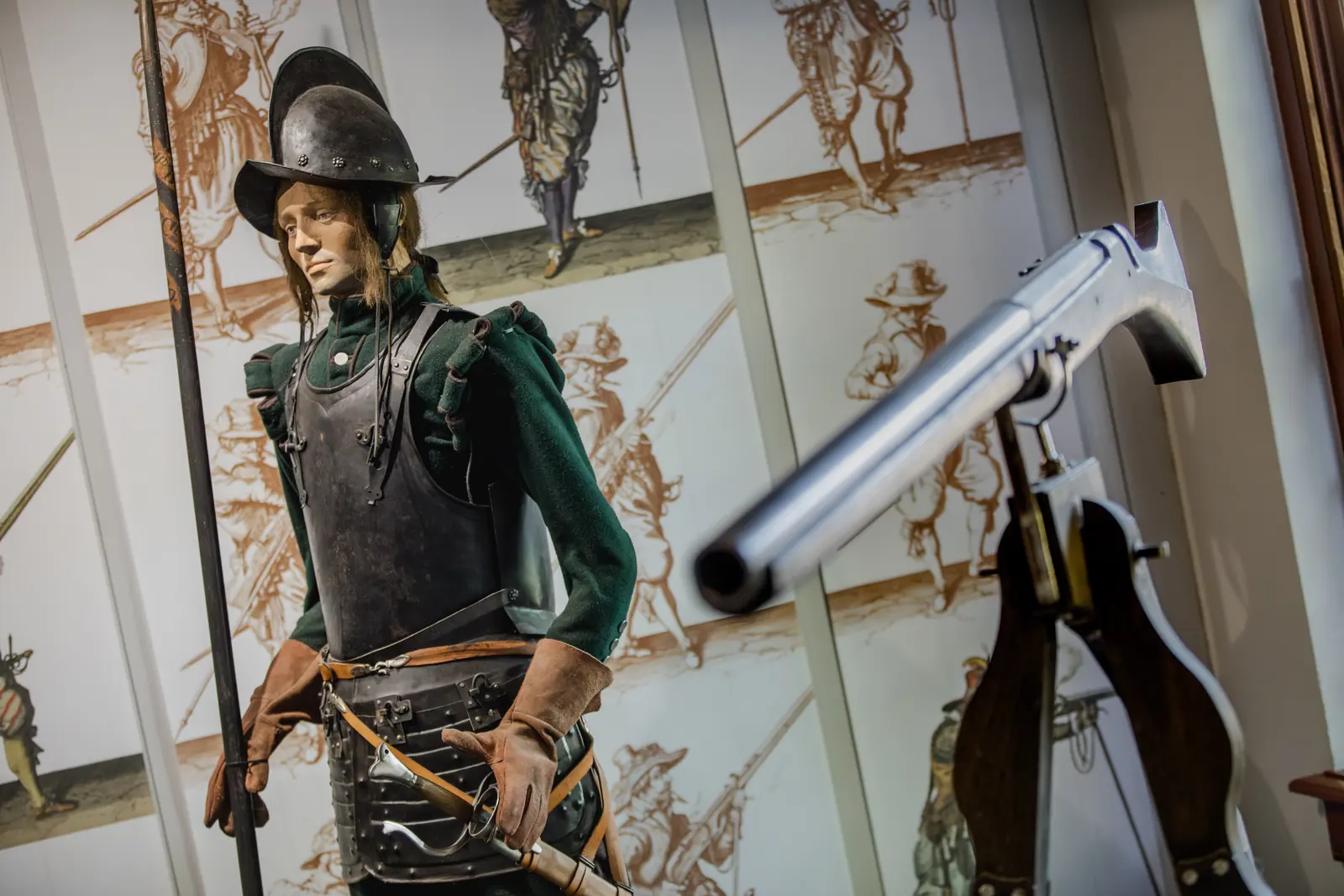 Un personnage en armure et casque tenant une pique, à côté d’un grand mousquet, au Museum De Baracquen.