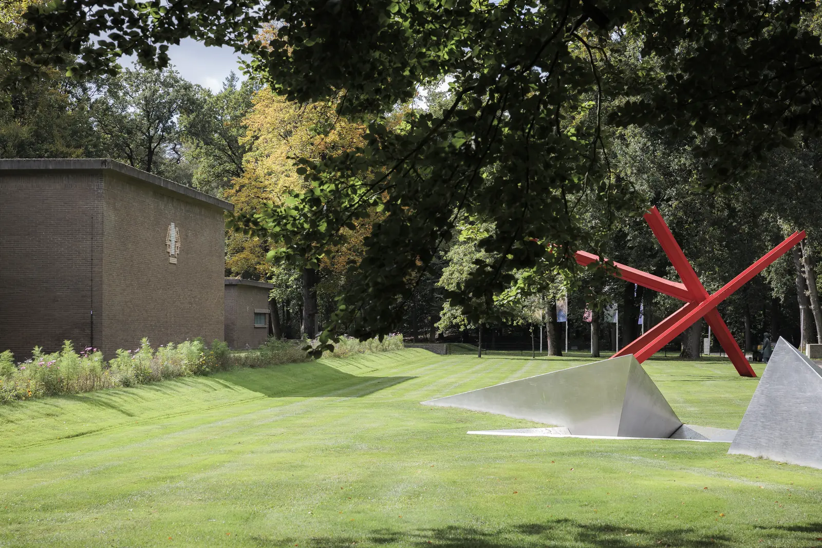 De voortuin van het Kröller-Müller Museum: een grasveld met een rood beeld, het lage museumgebouw en bomen.