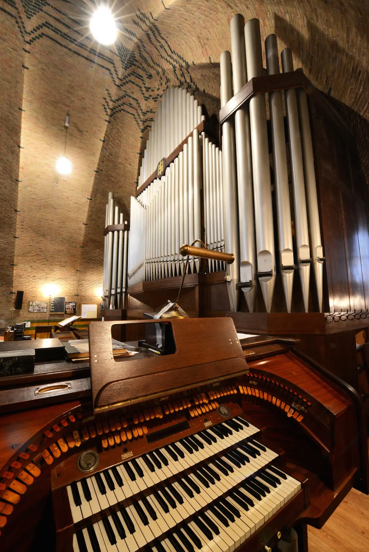 La console en bois de l’orgue avec trois claviers et des rangées de tirants de jeux, et derrière, de hauts tuyaux gris argent.