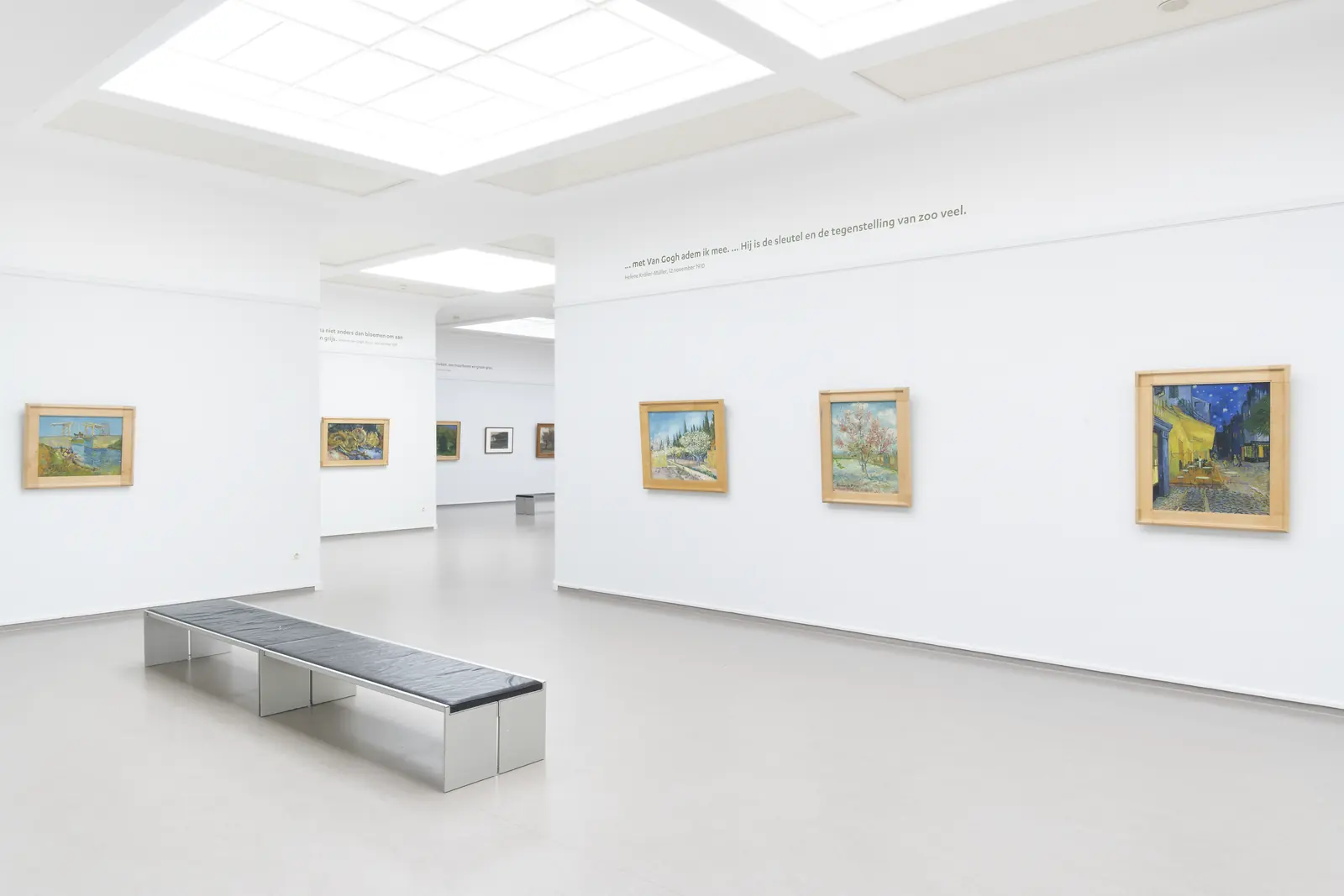 Een lichte museumzaal met schilderijen van Van Gogh aan witte wanden en een bank in het midden.