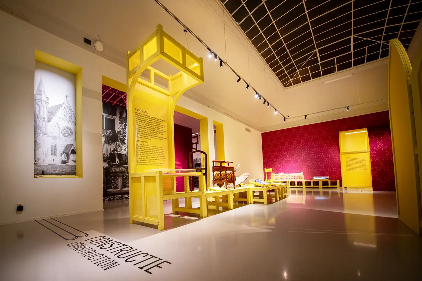 Tentoonstellingszaal met gele presentaties en objecten.