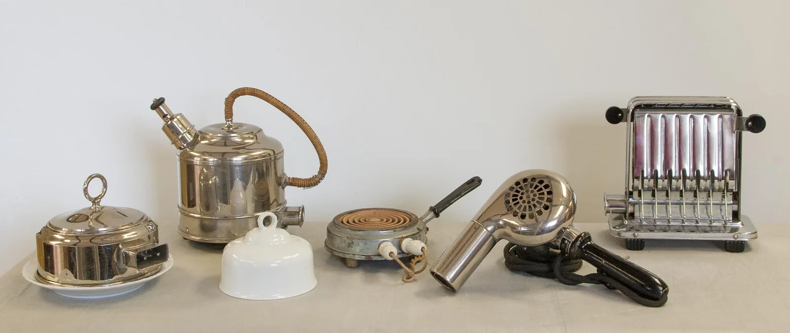 A group of historic electric household appliances, including a toaster and a hairdryer.