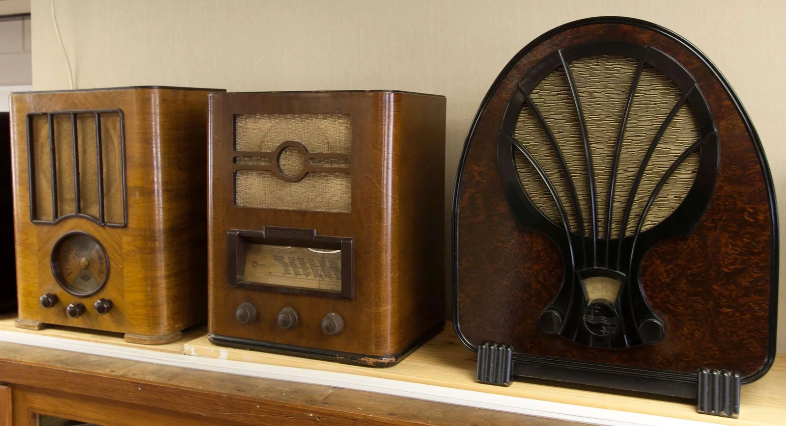 Three wooden radio sets on a shelf.