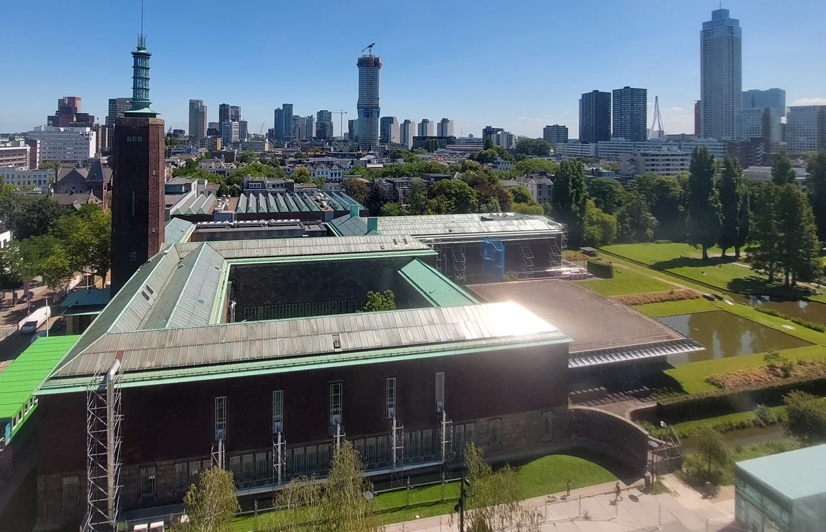 Museumgebouwen met binnenhoven en een tuin, van bovenaf gezien met de Rotterdamse skyline erachter.