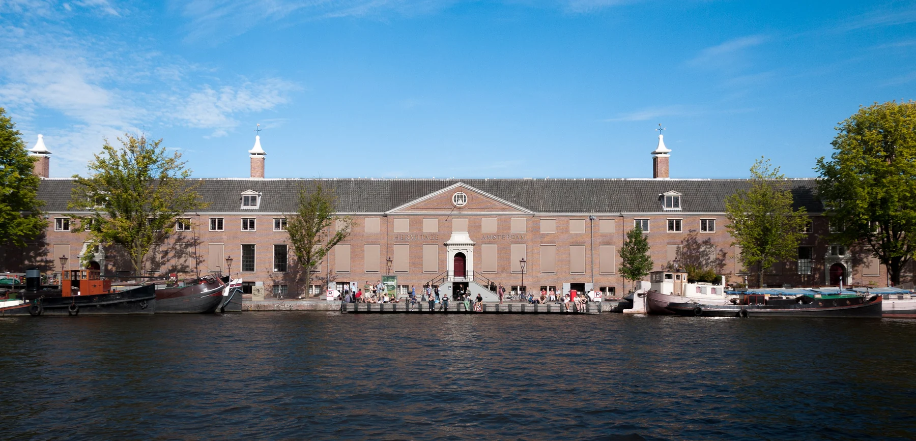 Long brick museum façade beside the Amstel, with boats and visitors along the quay.