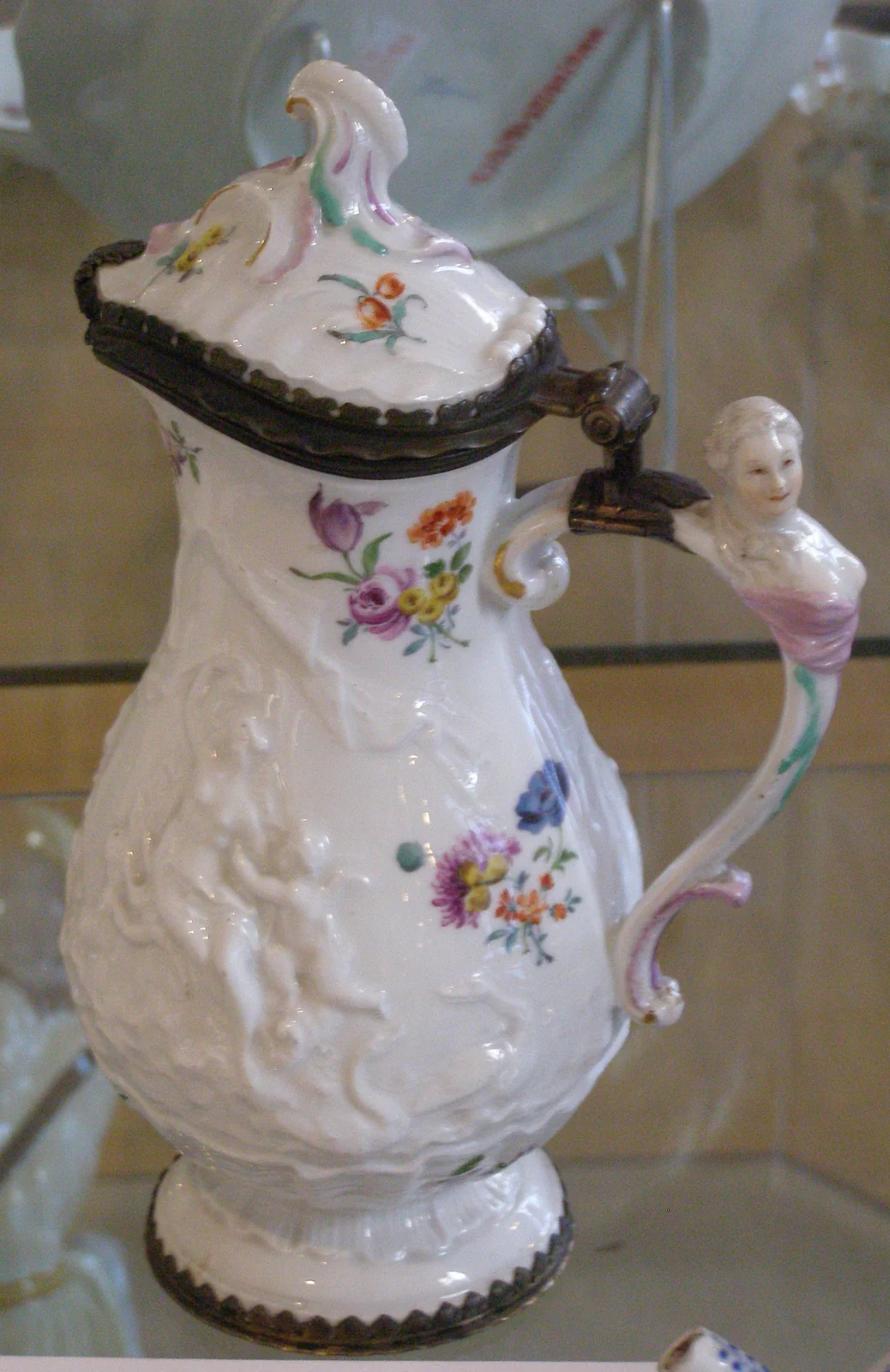 Weiße Kaffeekanne mit Blumen, Reliefdekor und einer menschlichen Figur am Griff.