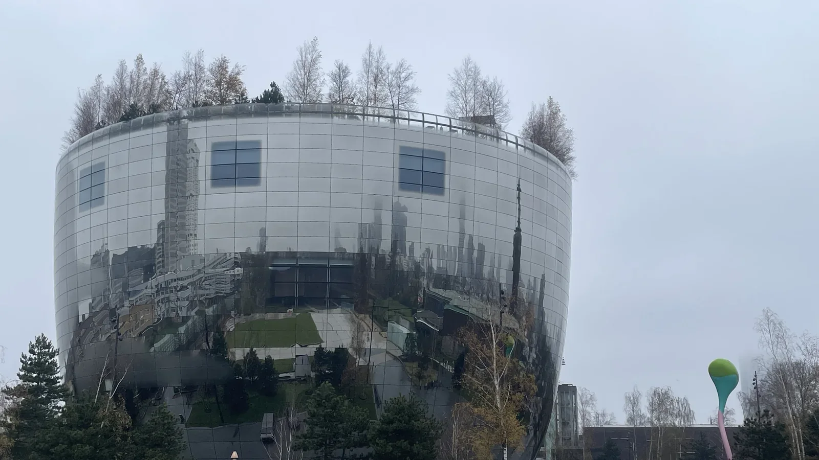 Das runde, spiegelnde Depot Boijmans Van Beuningen mit Bäumen auf dem Dach und Spiegelungen der Stadt.