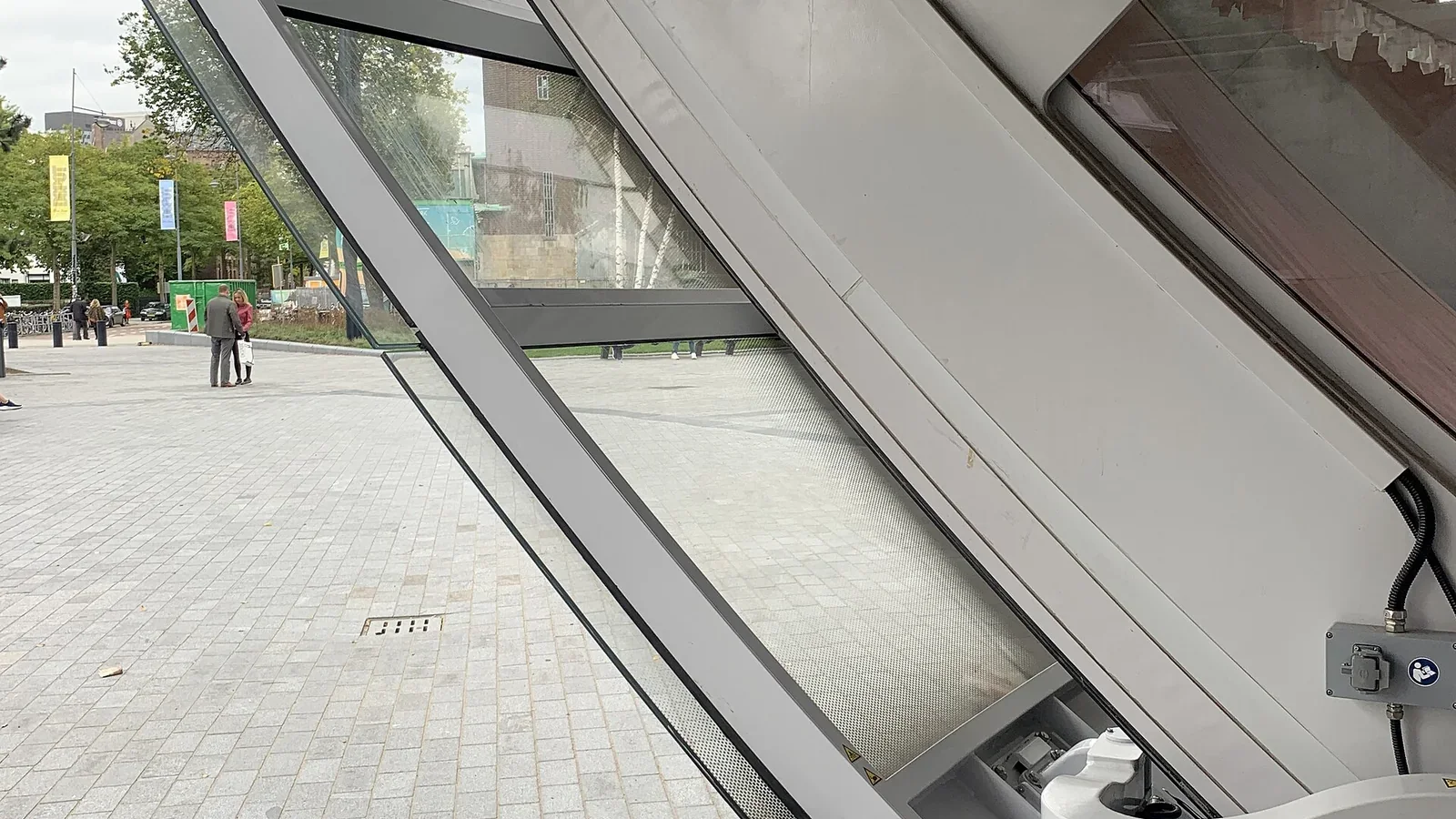 Schuine glazen en metalen constructie bij de ingang van het Depot, met zicht op het Museumpark en bezoekers buiten.