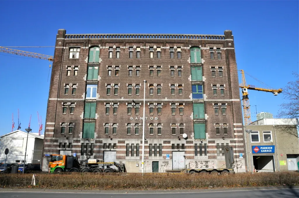 Brick façade of the Santos warehouse in Rotterdam with green shutters under a blue sky.