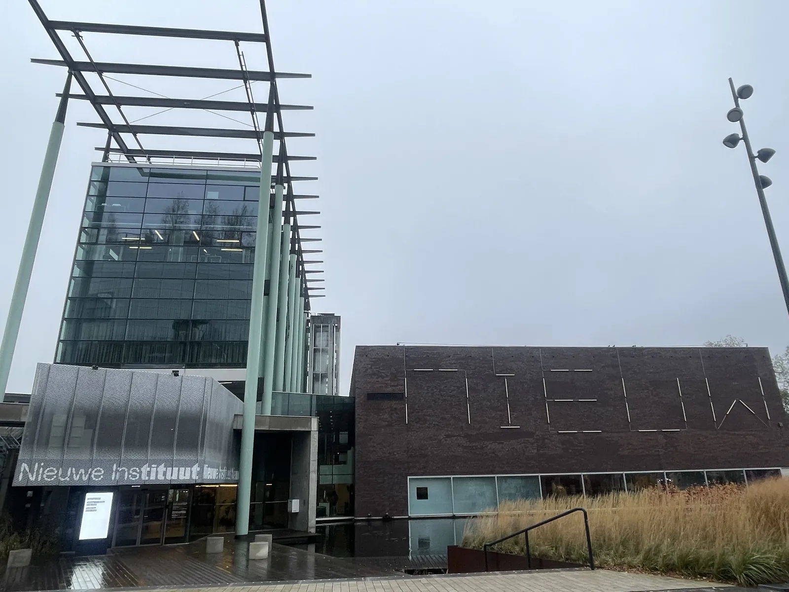 Moderne gevel van het Nieuwe Instituut met glazen toren, donkere zijgevel en de naam van het museum.