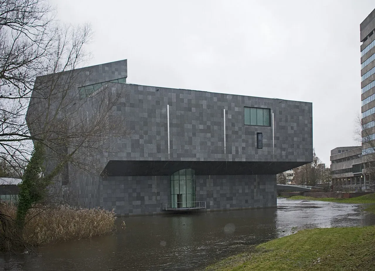 Dunkelgrauer Museumsneubau am Wasser.