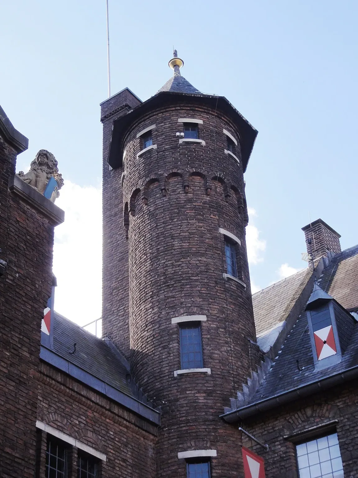 Bakstenen toren aan de binnenplaats van het kasteel, met vlagkleuren op de aangrenzende gevel.