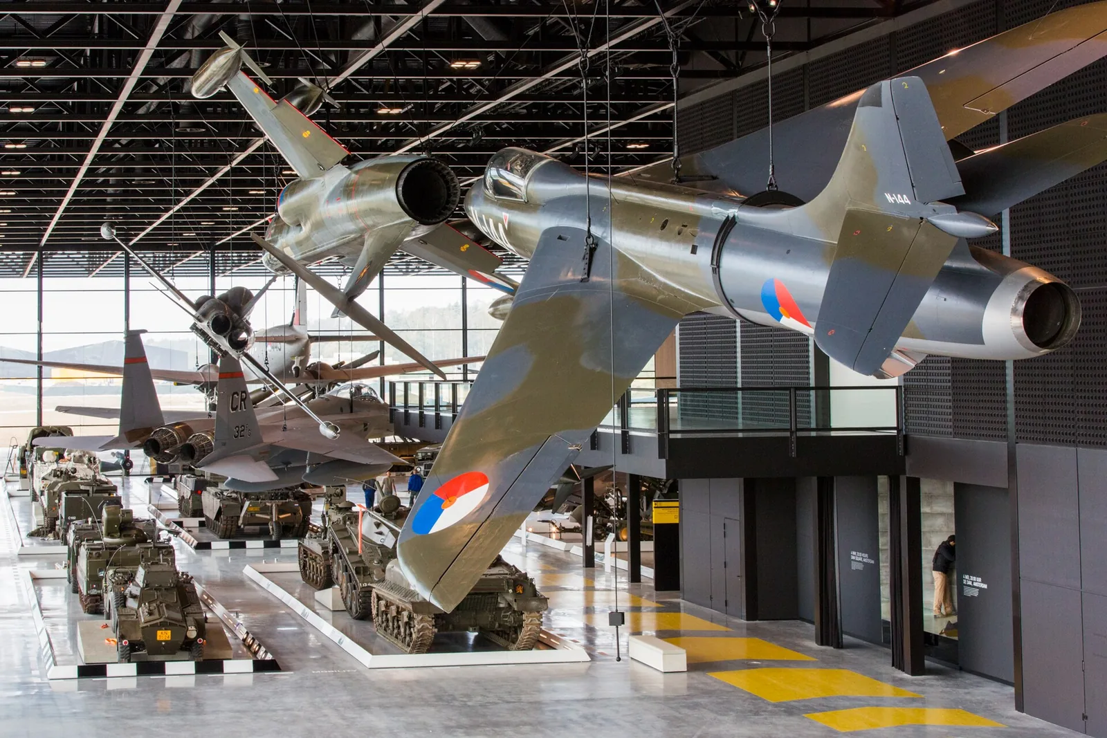 Aircraft hang above rows of military vehicles in the large Arsenal hall.