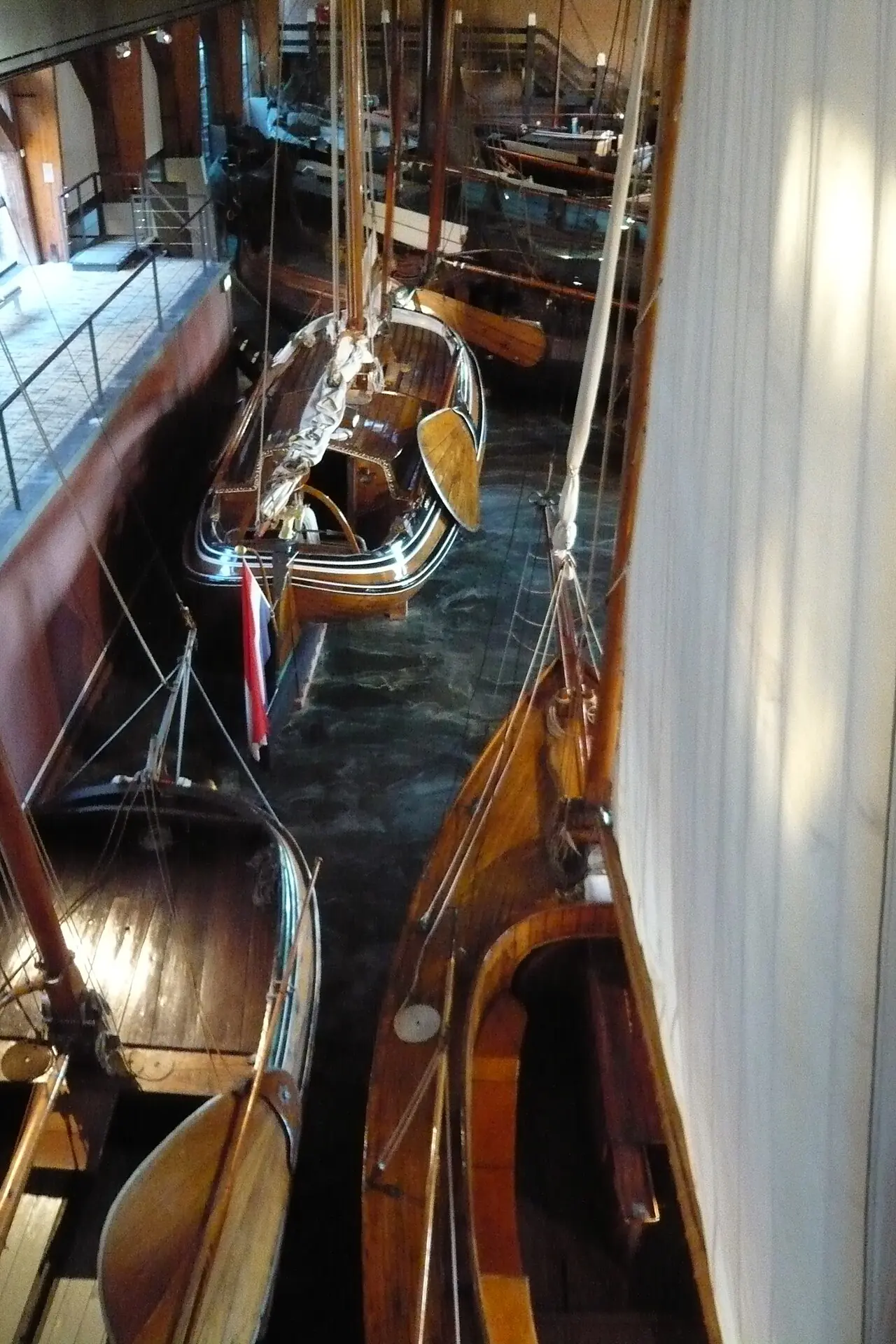 Wooden sailing boats stand close together in a tall, dim museum hall.