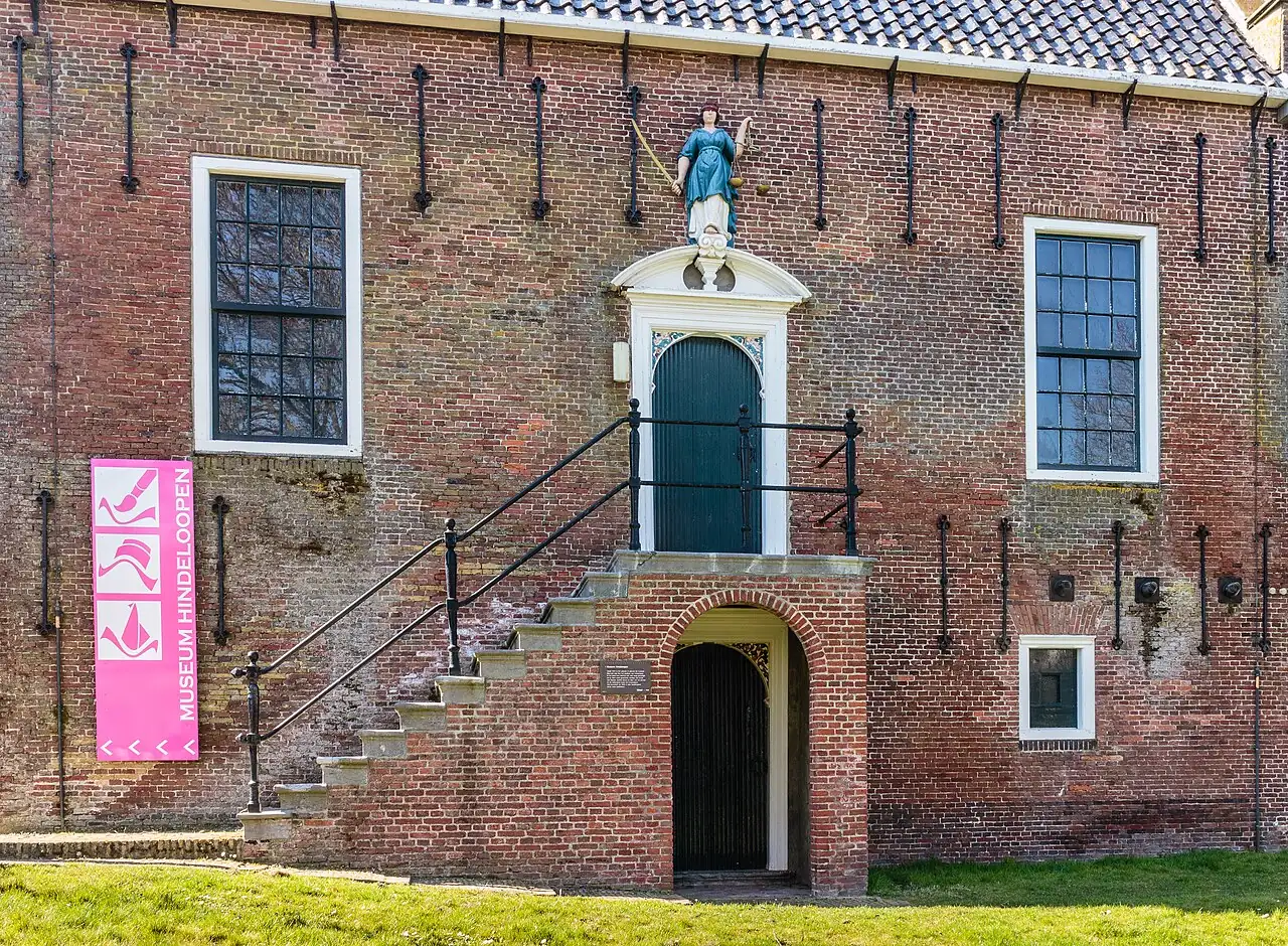 Bakstenen gevel van Museum Hindeloopen met trap, groene deur en roze museumbord.